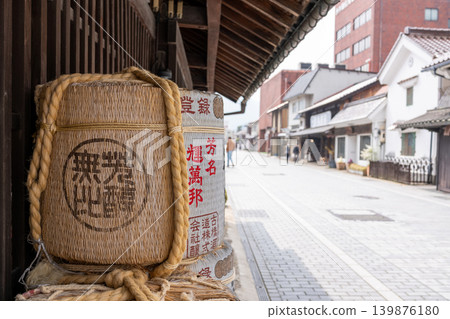 擺放在日本清酒釀酒廠入口處的清酒桶和歷史悠久的街景。 擺放在日本清酒釀酒廠入口處的清酒桶和歷史悠久的街景。 139876180