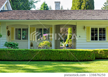 White Residential House Facade with Yellow Shutters and Trim Behind a Green Hedge White Residential House Facade with Yellow Shutters and Trim Behind a Green Hedge 139876250