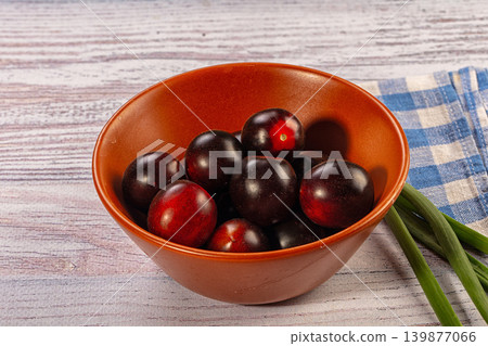 Black cherry tomatoes in terracotta bowl with green onions on rustic wood table 139877066