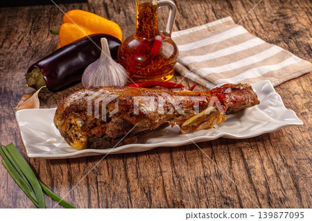 Delicious Roasted Meat Leg Plate Garnished with Fresh Vegetables and Chili Oil on Rustic Wooden Background Delicious Roasted Meat Leg Plate Garnished with Fresh Vegetables and Chili Oil on Rustic Wooden Background 139877095