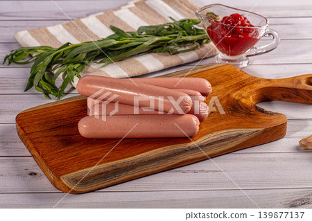 Raw sausages on wooden cutting board with ketchup and fresh tarragon Raw sausages on wooden cutting board with ketchup and fresh tarragon 139877137