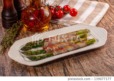 Savory grilled bacon wrapped asparagus spears on white platter with fresh herbs and tomatoes Savory grilled bacon wrapped asparagus spears on white platter with fresh herbs and tomatoes 139877177