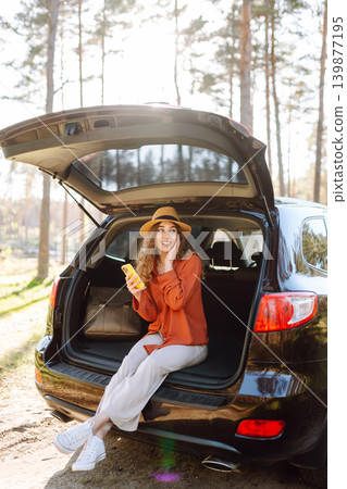 Beautiful woman sits in the trunk of a car outdoor and uses a smartphone. Active life. Beautiful woman sits in the trunk of a car outdoor and uses a smartphone. Active life. 139877195