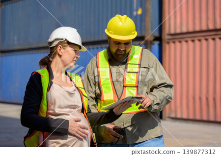 Diverse logistics team with pregnant female manager and male colleague worker reviewing data on tablet at shipping container yard port Diverse logistics team with pregnant female manager and male colleague worker reviewing data on tablet at shipping container yard port 139877312