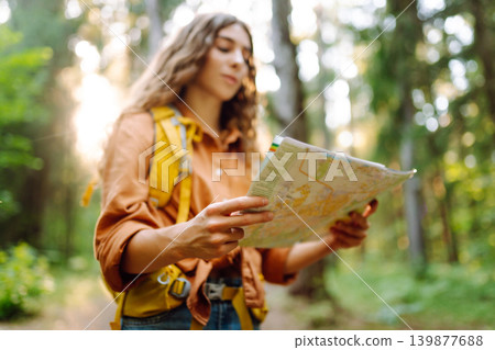 A traveler woman stands in a lush forest, examining a map with a focused expression 139877688