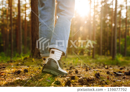 Feet of an adult wearing boots to travel walking in a green forest. Travel and hiking. Feet of an adult wearing boots to travel walking in a green forest. Travel and hiking. 139877702