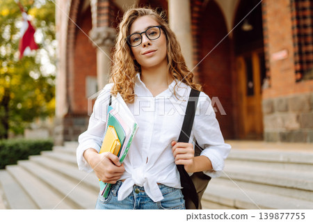 Female student woman holds several colorful notebooks near university building. Education concept. Female student woman holds several colorful notebooks near university building. Education concept. 139877755