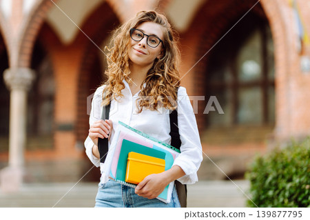 Female student woman holds several colorful notebooks near university building. Education concept. 139877795
