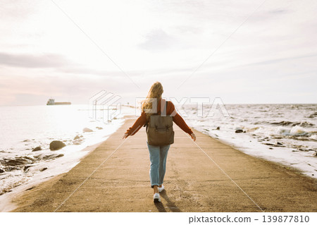 Woman enjoying breezy day near vibrant red lighthouse at sunset. Travel, weekend, lifestyle concept. Woman enjoying breezy day near vibrant red lighthouse at sunset. Travel, weekend, lifestyle concept. 139877810