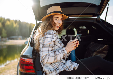 Happy woman with phone in hand sits in trunk of car. Concept of technology, adventure, travel by car 139877940