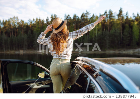 Joyful traveler embraces nature at sunset by lakeside with open car door, freedom, adventure. Joyful traveler embraces nature at sunset by lakeside with open car door, freedom, adventure. 139877943