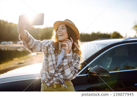Happy woman on vacation taking selfie photo with smartphone near car. Stylish model on a car trip. Happy woman on vacation taking selfie photo with smartphone near car. Stylish model on a car trip. 139877945