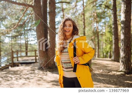 A cheerful young woman in a yellow jacket enjoying a sunny day by the lake. Trips. Active lifestyle. 139877969