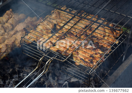 Grilled meat skewers on a barbecue grill. Smoke rises from the cooking food. Juicy pieces of meat are arranged in a metal grilling basket. Grilled meat skewers on a barbecue grill. Smoke rises from the cooking food. Juicy pieces of meat are arranged in a metal grilling basket. 139877982