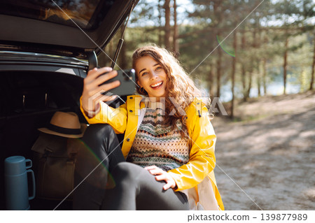 Woman is resting in trunk of car and taking selfie. Lifestyle, travel, tourism, nature, active life. Woman is resting in trunk of car and taking selfie. Lifestyle, travel, tourism, nature, active life. 139877989