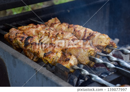 Grilled chicken skewers on a barbecue grill. The meat is golden brown and sizzling, surrounded by smoke. A delicious outdoor cooking scene. Grilled chicken skewers on a barbecue grill. The meat is golden brown and sizzling, surrounded by smoke. A delicious outdoor cooking scene. 139877997