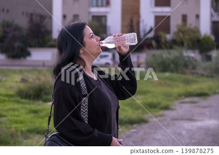 Woman Drinking Water from Plastic Bottle. Woman Drinking Bottled Water Outdoors. Woman Drinking Water from Plastic Bottle. Woman Drinking Bottled Water Outdoors. 139878275