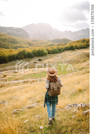 Back view. Travel woman explores scenic mountain landscape during in open field. Enjoying mountains Back view. Travel woman explores scenic mountain landscape during in open field. Enjoying mountains 139878366