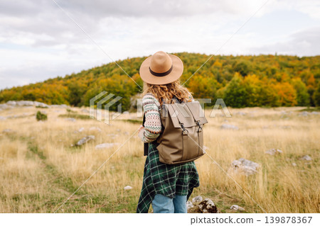 Back view. Travel woman explores scenic mountain landscape during in open field. Enjoying mountains Back view. Travel woman explores scenic mountain landscape during in open field. Enjoying mountains 139878367