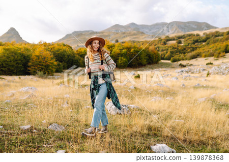 Young woman enjoys sunny afternoon in mountains while sitting on rocks. Tourism. Active lifestyle. 139878368