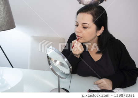Woman Applying Makeup in Front of Mirror. Woman Applying Makeup in Front of Mirror. 139878381
