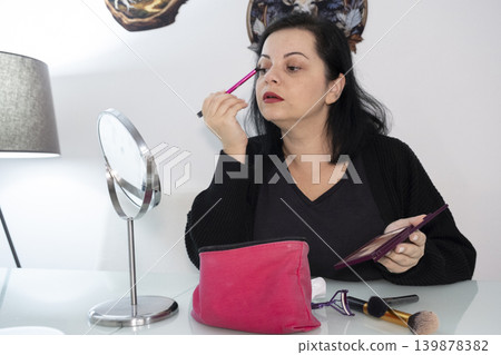 Woman Applying Makeup in Front of Mirror. 139878382