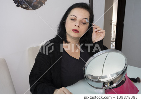 Woman Applying Makeup in Front of Mirror. Woman Applying Makeup in Front of Mirror. 139878383