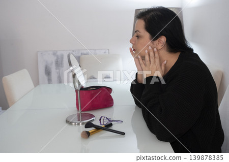 Woman Applying Makeup in Front of Mirror. Woman Applying Makeup in Front of Mirror. 139878385