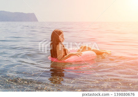 Girl inflatable sea floating on a pink rubber ring in clear coastal water during sunset for summer vacation concept Girl inflatable sea floating on a pink rubber ring in clear coastal water during sunset for summer vacation concept 139880676