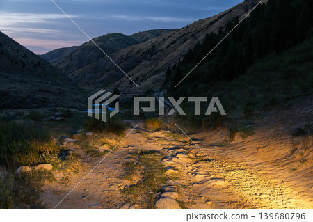 Dirt Road in Mountain Valley at Twilight illuminated with Headlights in Kyrgyzstan Dirt Road in Mountain Valley at Twilight illuminated with Headlights in Kyrgyzstan 139880796