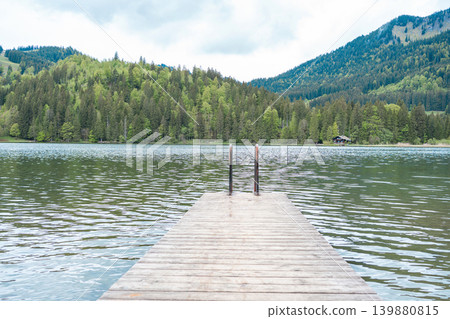 View from a wooden dock onto the calm surface of a mountain reservoir. Symmetry, perspective, travel concept, solitude, meditation, and serenity. View from a wooden dock onto the calm surface of a mountain reservoir. Symmetry, perspective, travel concept, solitude, meditation, and serenity. 139880815
