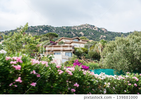 Steep, rocky mountains and tropical-style houses under a cloudy sky – on the French island of Corsica in the Mediterranean Sea. Steep, rocky mountains and tropical-style houses under a cloudy sky – on the French island of Corsica in the Mediterranean Sea. 139881000