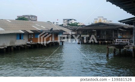 Wooden stilt houses built over calm water near a pier in a traditional coastal fishing village in Thailand. Waterfront village concept Wooden stilt houses built over calm water near a pier in a traditional coastal fishing village in Thailand. Waterfront village concept 139881526