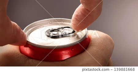 Cola or soda can opening. Close up of hand open aluminum beverage can with pull tab. Refreshing Cola or soda carbonated soft drink container with metal texture condensation droplets and easy open lid 139881668