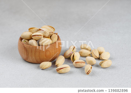 Little wooden bowl with salted pistachio nuts and scattered seeds on gray background close up Little wooden bowl with salted pistachio nuts and scattered seeds on gray background close up 139882896
