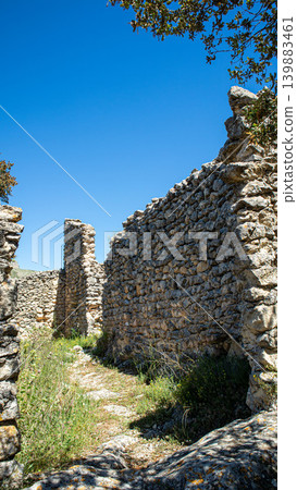 The site shows old stone walls from the abandoned Moorish village of Atzuvieta in Vall de Alcala, Spain. The location is under a clear, blue sky. Greenery grows between the stones. 139883461