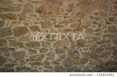 An old rustic stone wall made of irregular brown clay bricks and mortar typical of Mediterranean architecture. The wall has a weathered look. 139883462