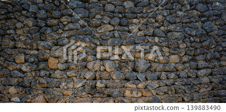 A dry stone wall stands firm in the countryside, built from rough and weathered rocks. This wall showcases traditional building techniques in a rural European setting, clear in broad daylight. A dry stone wall stands firm in the countryside, built from rough and weathered rocks. This wall showcases traditional building techniques in a rural European setting, clear in broad daylight. 139883490