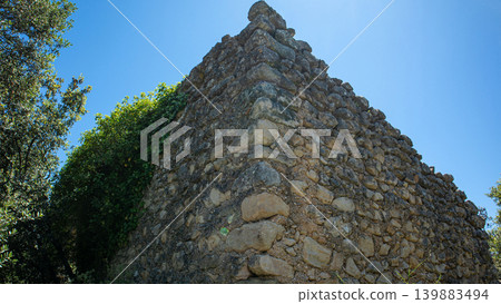 View shows a stone structure covered in ivy at the Atzuvieta archaeological site. The sunlight shines on the historic stones. Nature surrounds the ancient site. View shows a stone structure covered in ivy at the Atzuvieta archaeological site. The sunlight shines on the historic stones. Nature surrounds the ancient site. 139883494