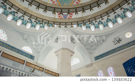 The interior of a mosque displays muqarnas vaulting, marble columns, and sacred calligraphy. The bright background highlights the architectural details in this worship space. The interior of a mosque displays muqarnas vaulting, marble columns, and sacred calligraphy. The bright background highlights the architectural details in this worship space. 139883622