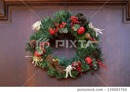 Traditional evergreen Christmas wreath decorated with ornaments on wooden entrance door Traditional evergreen Christmas wreath decorated with ornaments on wooden entrance door 139883768