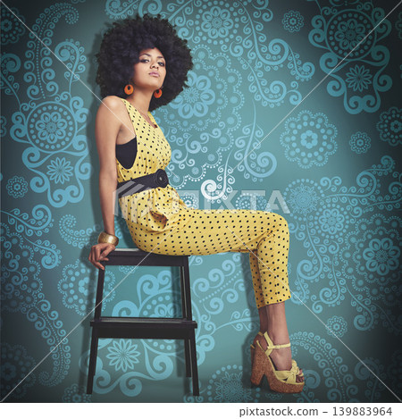 Portrait, young woman and fashion in 70s retro colour jumpsuit and sitting on chair. African trend, elegant model pretty in vintage outfit, big curly hair and wedge heels on cool pattern background Portrait, young woman and fashion in 70s retro colour jumpsuit and sitting on chair. African trend, elegant model pretty in vintage outfit, big curly hair and wedge heels on cool pattern background 139883964