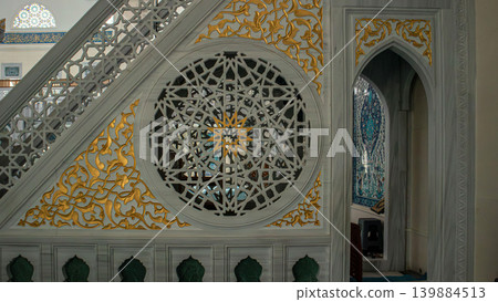 The minbar stands in bright mosque, featuring intricate stone work and gold leaf accents. Traditional star patterns fill the details, reflecting cultural artistry in a sacred space. The minbar stands in bright mosque, featuring intricate stone work and gold leaf accents. Traditional star patterns fill the details, reflecting cultural artistry in a sacred space. 139884513