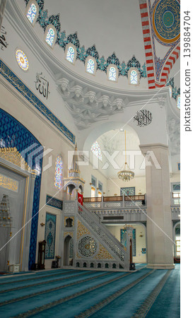 The mosque interior shows a marble minbar with golden accents. A Turkish flag is displayed against arched galleries. The space is designed for prayer and reflection. The mosque interior shows a marble minbar with golden accents. A Turkish flag is displayed against arched galleries. The space is designed for prayer and reflection. 139884704