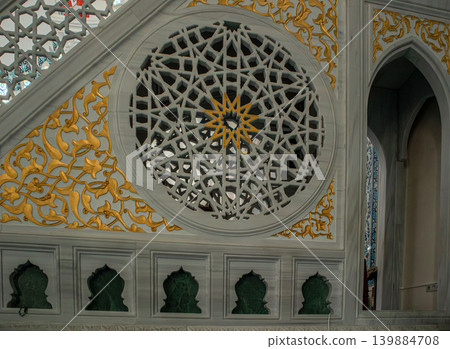 Visitors observe detailed stone carvings and unique arch designs within a modern mosque filled with bright light. The interior showcases artistic craftsmanship and cultural expression. 139884708