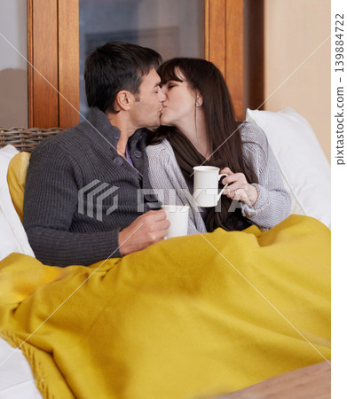 Love, hug and couple kissing on a sofa with trust, support or bonding with coffee and blanket at home. Mouth, embrace or people in living room with security, safety or romance while chilling with tea Love, hug and couple kissing on a sofa with trust, support or bonding with coffee and blanket at home. Mouth, embrace or people in living room with security, safety or romance while chilling with tea 139884722