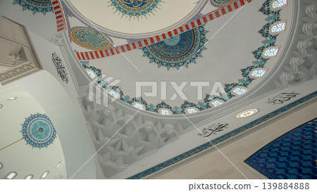 The image shows a low angle view of a mosque dome featuring geometric patterns and Arabic calligraphy. Architectural elements like muqarnas highlight the design. This setting is bright and inviting. The image shows a low angle view of a mosque dome featuring geometric patterns and Arabic calligraphy. Architectural elements like muqarnas highlight the design. This setting is bright and inviting. 139884888