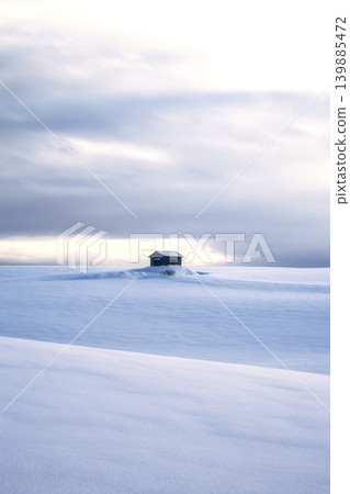 A clean winter scene of a small cabin standing alone in the vast, endless snowfield. 139885472