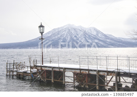 Hokkaido - Winter: A pier bridge and retro streetlights at Lake Shikotsu, with snow-covered mountain ranges. Hokkaido - Winter: A pier bridge and retro streetlights at Lake Shikotsu, with snow-covered mountain ranges. 139885497