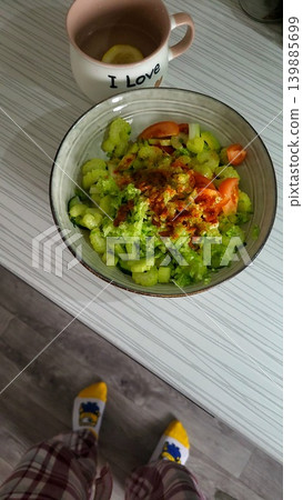 Nutritious bowl of green salad with tomatoes and a cup on a wooden surface, healthy organic lunch lifestyle. Nutritious bowl of green salad with tomatoes and a cup on a wooden surface, healthy organic lunch lifestyle. 139885699
